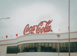 Exterior view of Coca-Cola factory with iconic red sign atop the modern building.